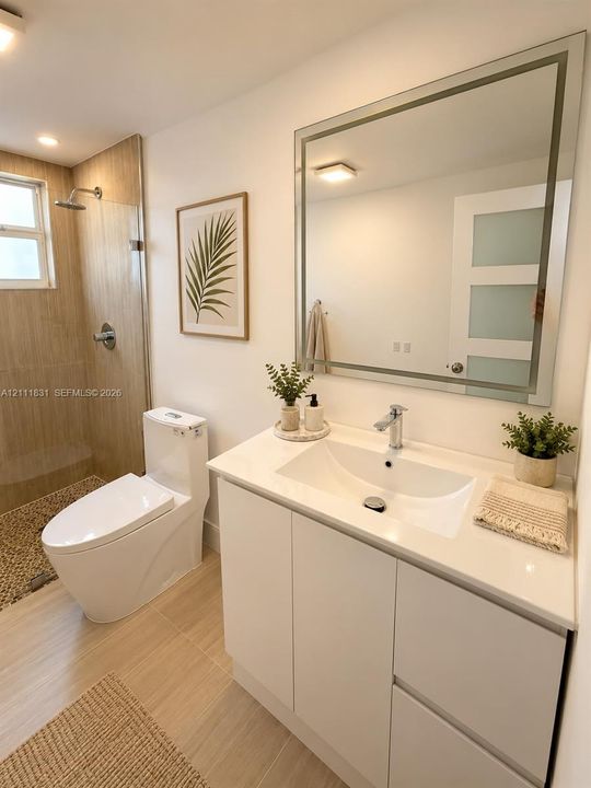 White vanity cabinet with an integrated sink and light-toned countertop, framed mirror, walk-in shower with tile surround, and neutral floor tiling