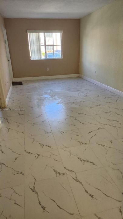 Large-format, veined tile flooring throughout, neutral interior wall paint, and a single-pane window