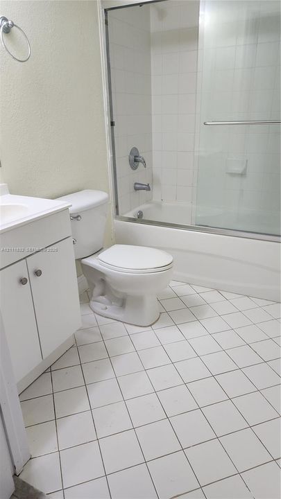 Bathroom featuring a white vanity cabinet, a shower and tub combination with a glass sliding enclosure, ceramic tile flooring, and a wall-mounted ring towel holder