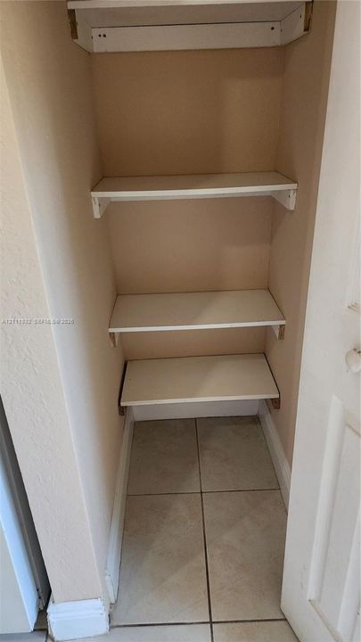 Built-in storage closet featuring three white shelves and tiled flooring