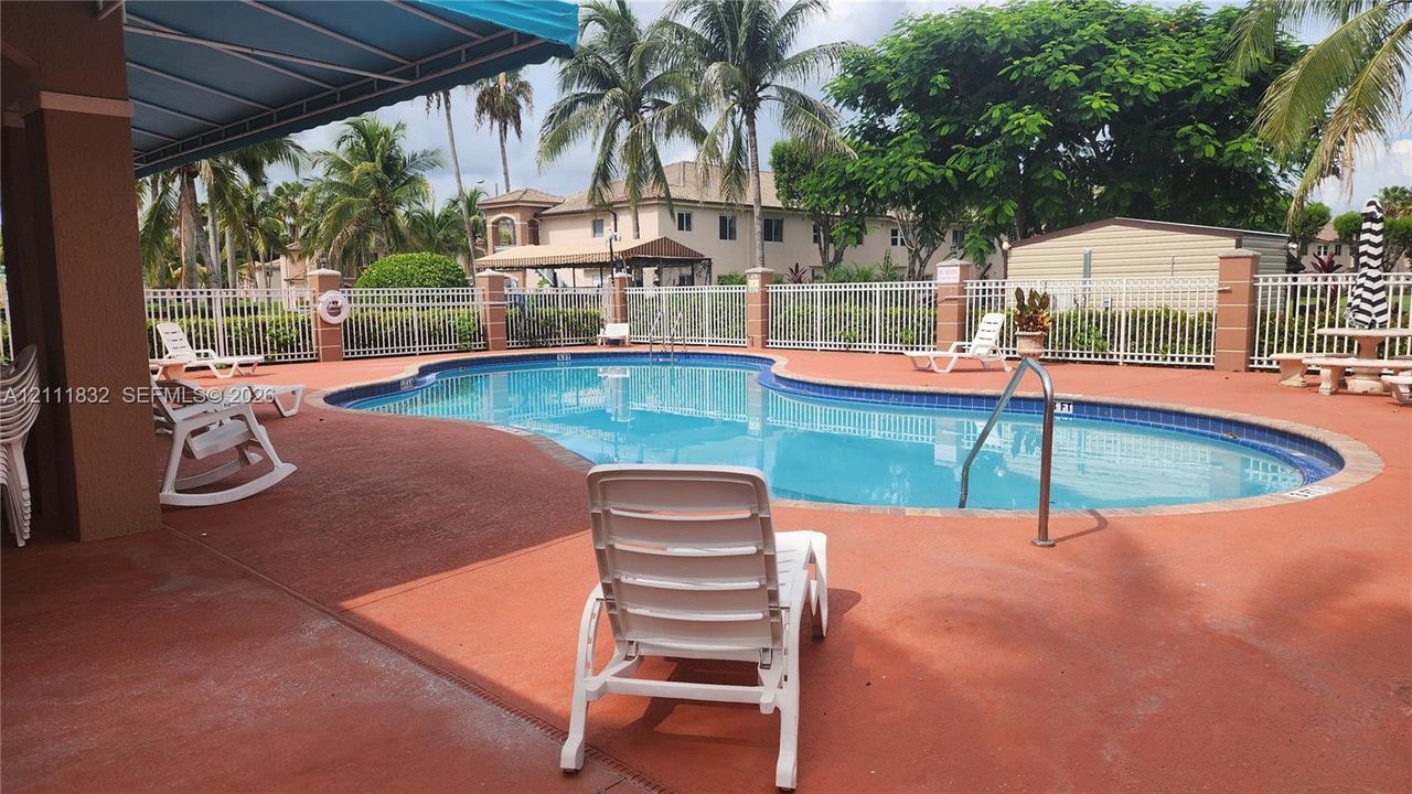 In-ground swimming pool with tile border, paver-style decking, white metal perimeter fencing, and retractable fabric awning