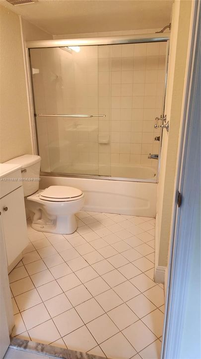 Full bathroom featuring a tub-shower combination with a glass sliding enclosure, ceramic wall tile surround, white vanity, and diagonal ceramic floor tiling