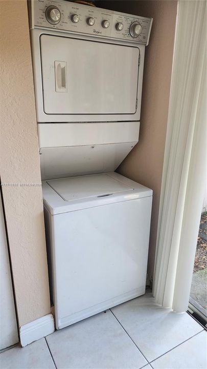White stacked laundry unit featuring a top-load washer and a control panel with tactile rotary dials, installed within a tiled-floor alcove