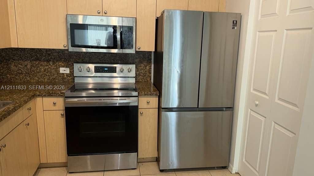 Kitchen featuring light-finish cabinetry, stone-surface countertops, and a suite of stainless steel appliances including a multi-door refrigerator, electric range, and over-the-range microwave