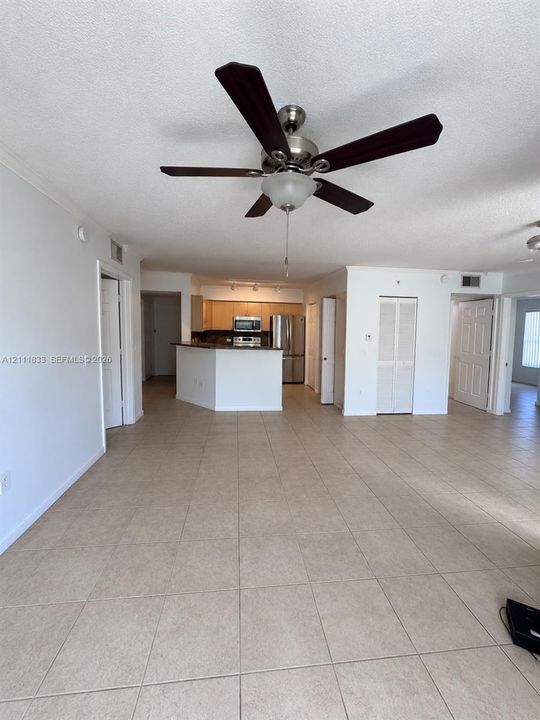 Open floor plan featuring large-format tile flooring, a central ceiling fan, a kitchen island with a breakfast bar, and stainless steel appliances