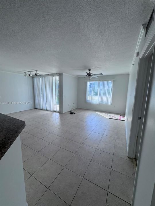 Open-concept living space featuring large-format ceramic tile flooring, a ceiling fan with integrated lighting, track lighting, and vertical window blinds