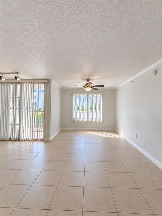 Interior space featuring neutral tile flooring, crown molding, a ceiling fan with integrated lighting, and sliding glass doors with vertical blinds