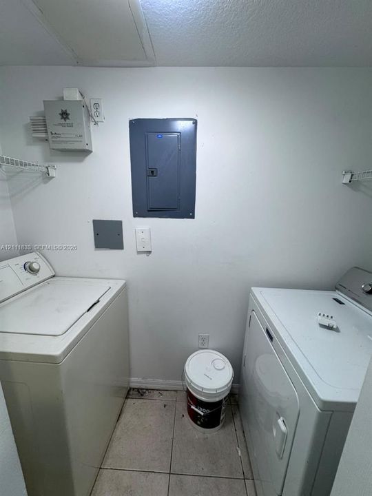 Utility area featuring tiled flooring, wall-mounted electrical panel, and built-in wire shelving
