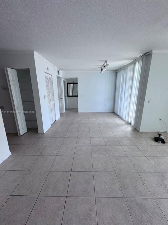 Open floor plan interior featuring large-format ceramic tile flooring, vertical window blinds, recessed track lighting, and built-in closet storage