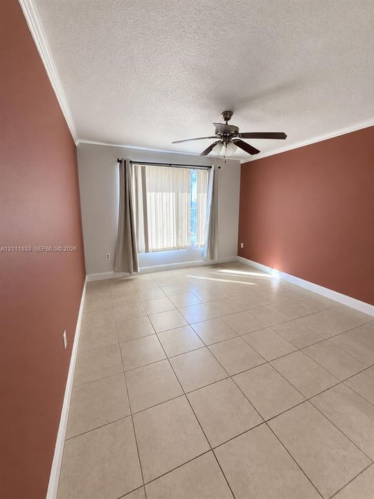 Spacious room featuring neutral ceramic tile flooring, a central ceiling fan with integrated lighting, and crown molding