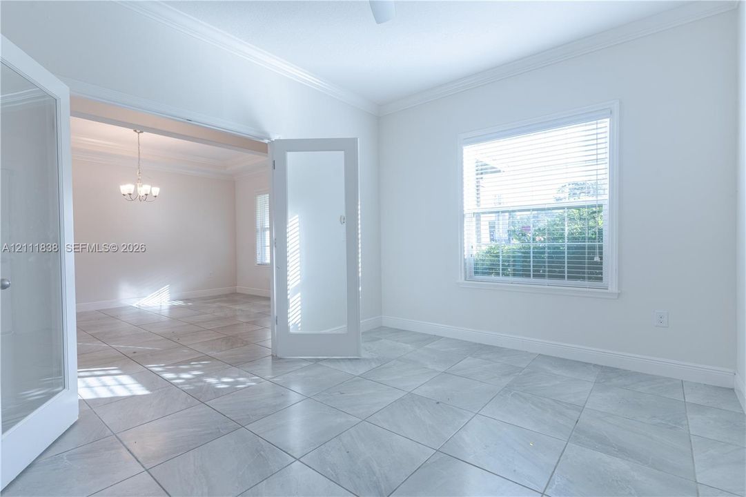 Large-format tile flooring, crown molding, double French doors, and multi-pane window