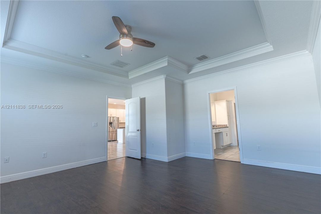 Tray ceiling, dark wood-finish flooring, and a ceiling-mounted light fixture with fan