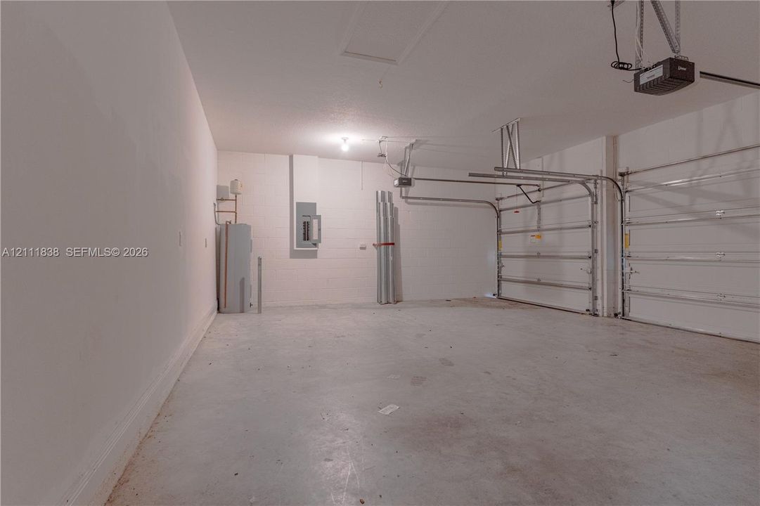 Multi-car garage featuring a concrete floor, two white sectional overhead doors, wall-mounted electrical panel, and an attached automatic garage door opener