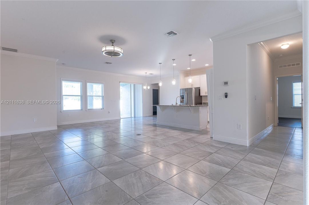 Open-concept interior featuring large-format stone-finish tile flooring, a kitchen island with stone countertop, multi-pendant lighting, and recessed ceiling fixtures