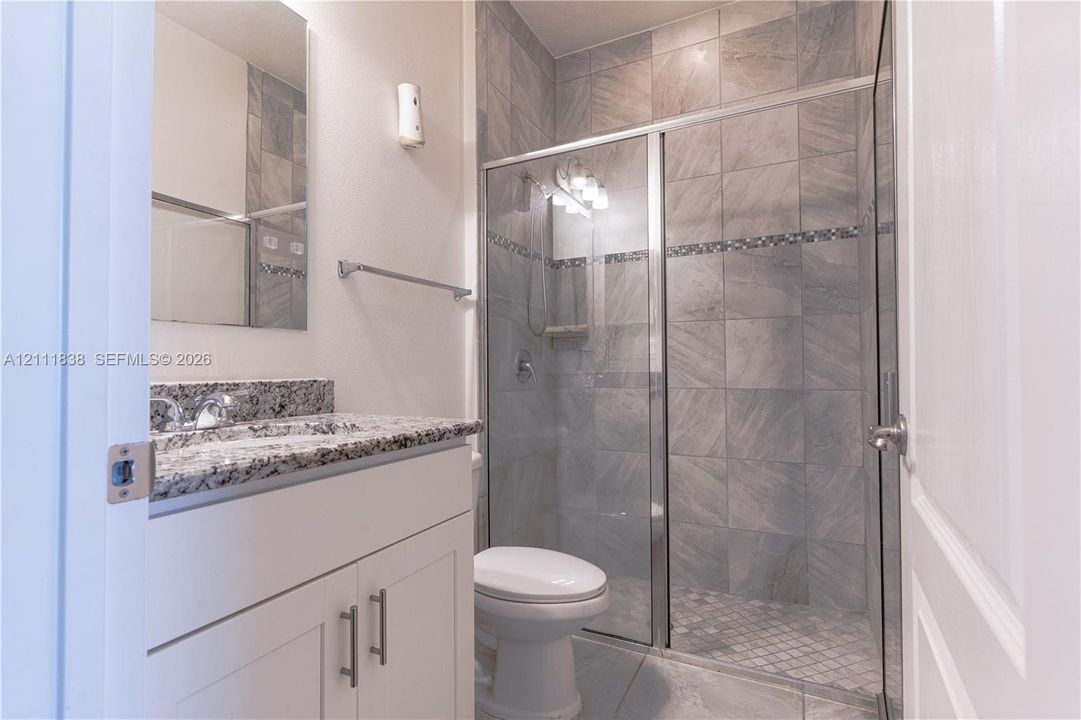Bathroom featuring a stone-top vanity with undermount sink, shower with glass enclosure, decorative tile inlay, and tiled flooring