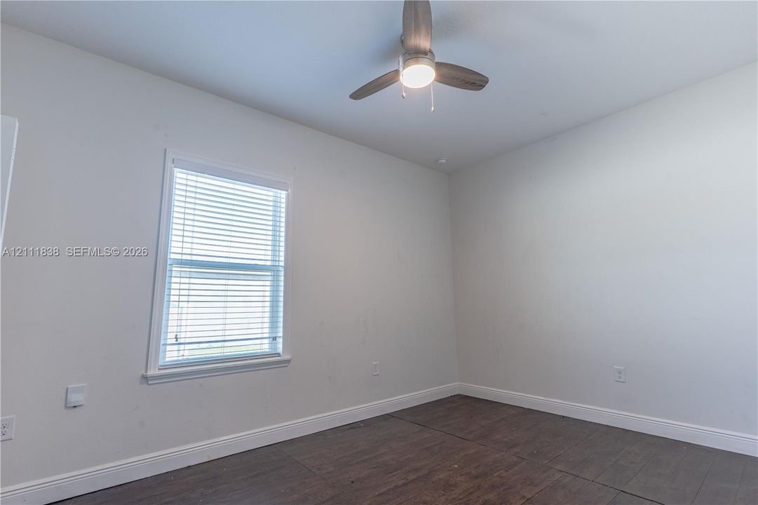 Room featuring wood-finish flooring, a single-light ceiling fan with gray blades, and a window with horizontal blinds
