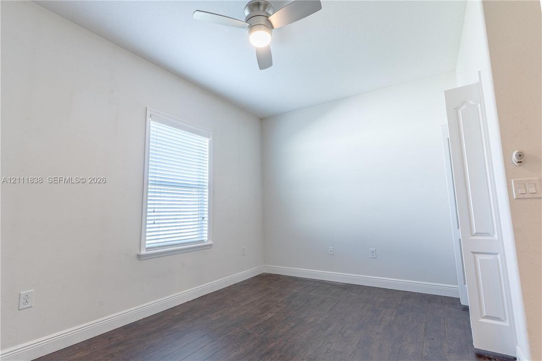 Interior space featuring wood-finish flooring, a neutral color palette, a single-hung window with horizontal blinds, and a brushed metal ceiling fan