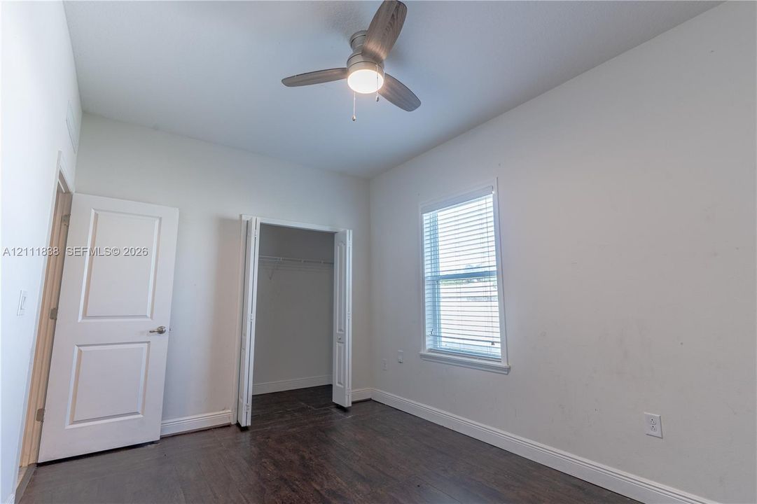 Room featuring wood-finish flooring, a ceiling fan with integrated lighting, a walk-in closet, and a window with blinds