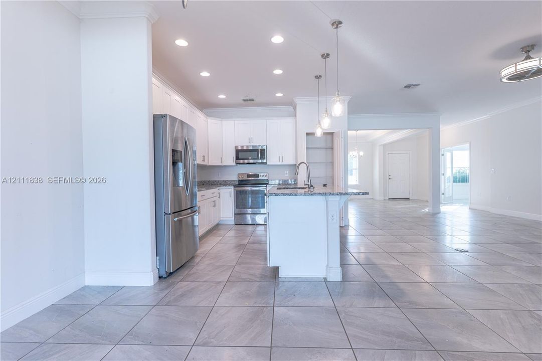 Kitchen featuring white cabinetry, stone countertops, stainless steel appliances, a center island with a sink, and tile flooring