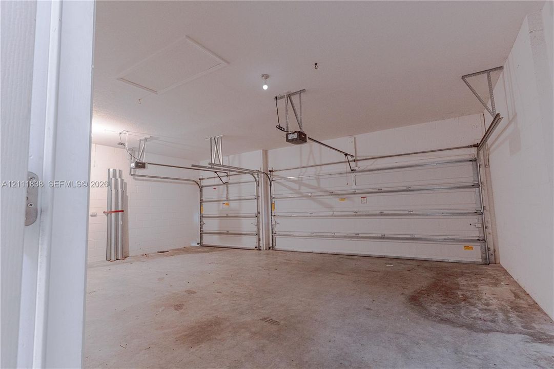 Two-car garage featuring automated sectional doors, concrete flooring, and an attic access hatch