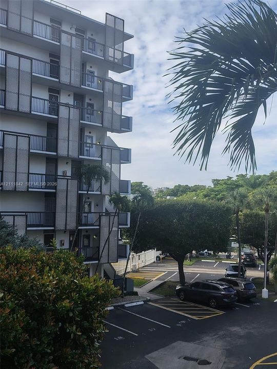 Multi-story building exterior featuring dark metal grid balcony privacy screens, private balconies, and asphalt surface parking lot