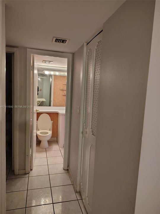 Hallway featuring light-toned ceramic tile flooring and bi-fold closet doors with decorative perforated metal panels