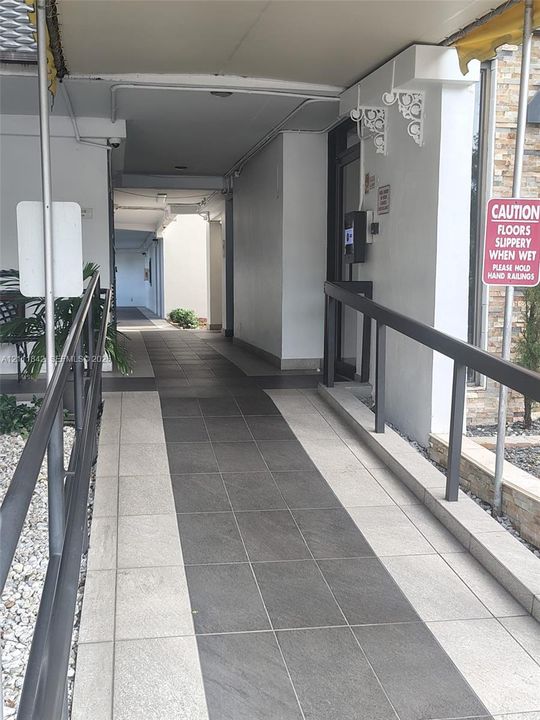 Covered exterior walkway featuring dual-tone tile flooring and metal handrails