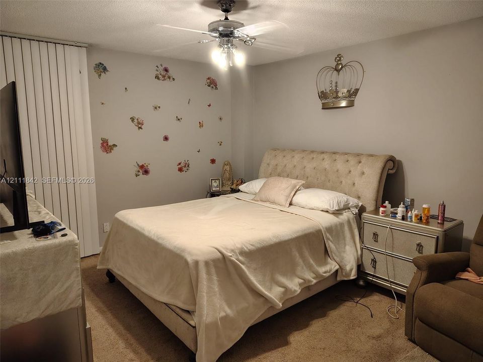 Neutral wall tones, carpeted flooring, vertical window blinds, and a central ceiling fan with multi-light fixture