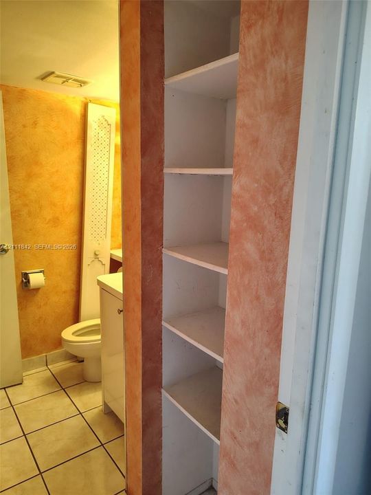 Built-in floor-to-ceiling storage shelving with a decorative faux-finish trim, ceramic tile flooring, and a white vanity cabinet