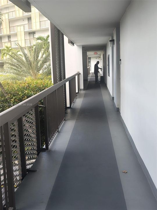 Exterior corridor featuring painted concrete flooring, metal railings with decorative mesh panels, and wall-mounted exterior lighting