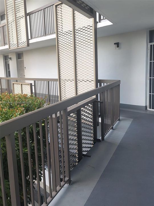 Exterior walkway featuring a metal railing, geometric privacy screens, and integrated wall-mounted lighting