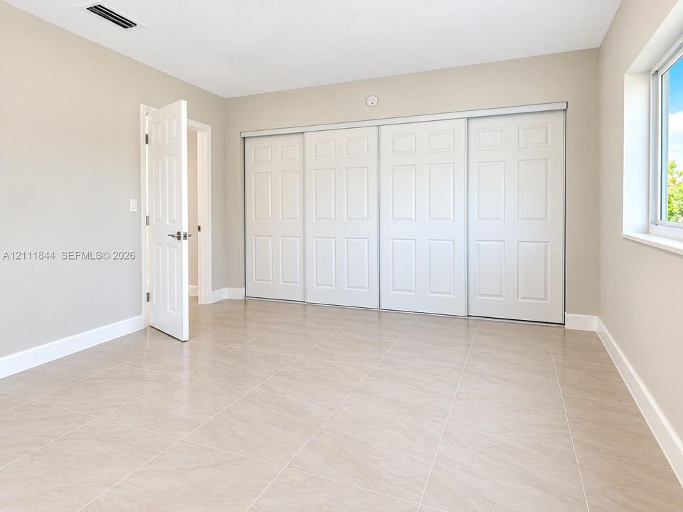 Neutral-toned room featuring large-format tile flooring, oversized four-panel sliding closet doors, and a single window