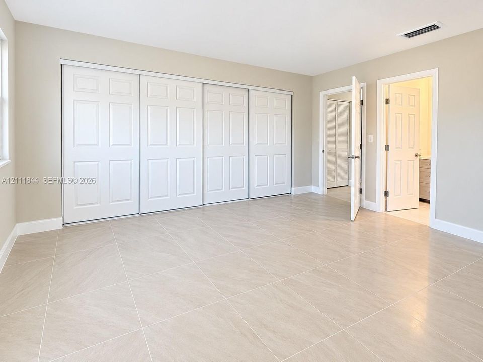 Neutral-toned interior space featuring light-colored stone-finish tile flooring, four-panel sliding closet doors, and traditional hinged doorways with brushed metal hardware