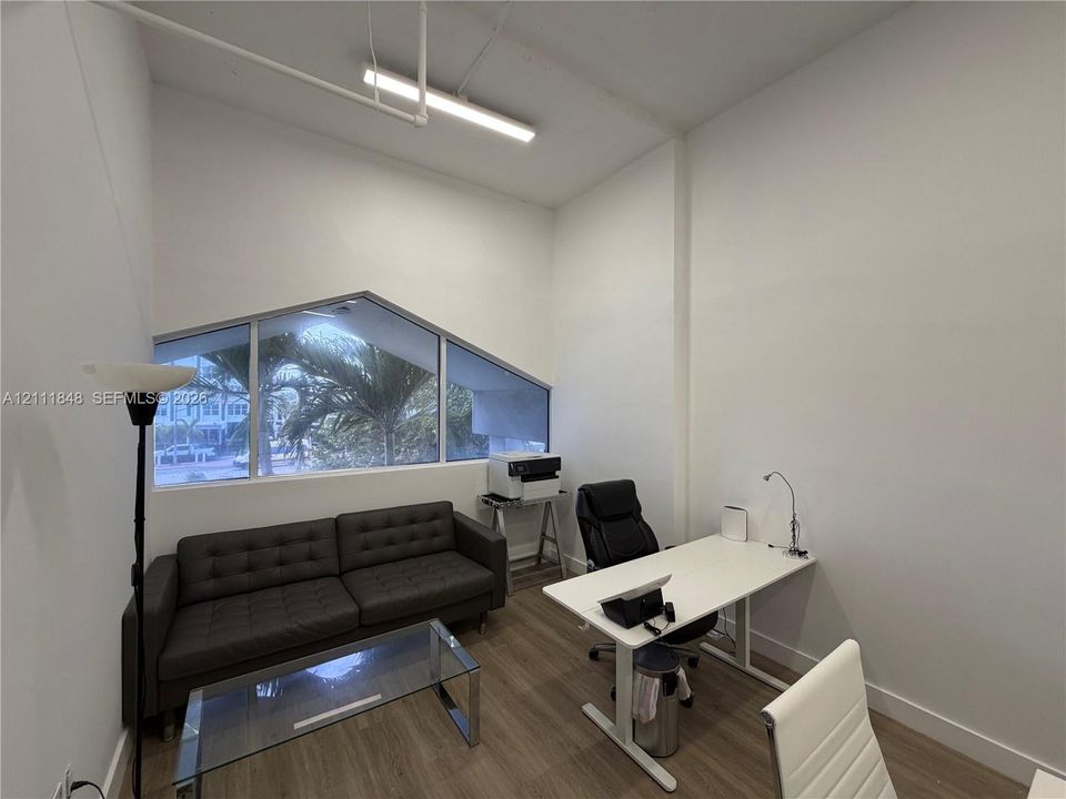 High-ceilinged room featuring wood-finish flooring, angled architectural window, and linear suspended lighting