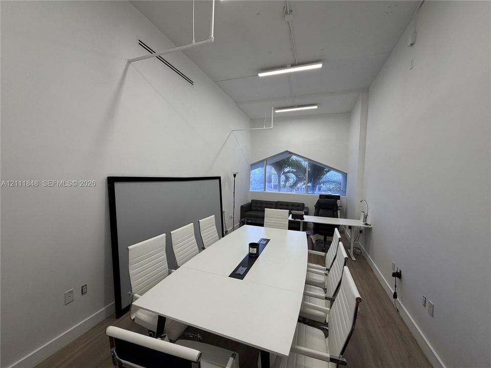 High-ceiling interior featuring wood-finish flooring, exposed piping, linear LED lighting, and a custom-shaped geometric window
