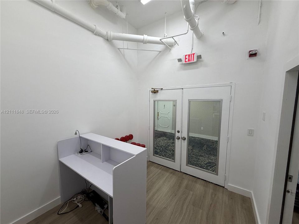 High-ceiling interior featuring wood-finish flooring, built-in desk, and double glass-panel doors