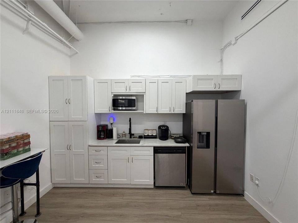 Kitchenette featuring white Shaker-style cabinetry, high-contrast matte black faucet, stone-finish countertops, stainless steel dishwasher, and matching side-by-side refrigerator