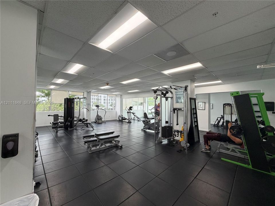 Fitness center featuring black rubberized flooring, drop ceiling with recessed fluorescent lighting, and extensive window coverage