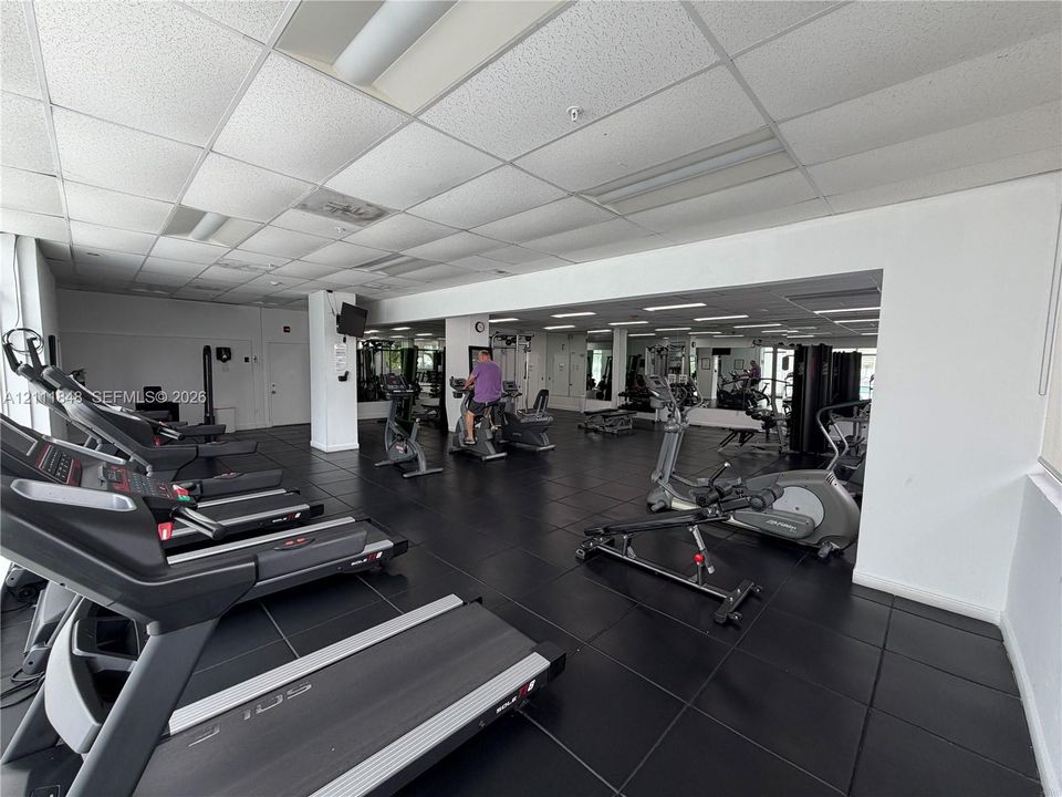 Fitness center featuring black rubber flooring, wall-to-wall mirrors, and a suspended drop ceiling