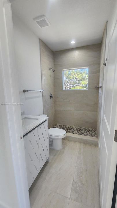 Bathroom featuring floor-to-ceiling large-format tile wall cladding, walk-in shower with pebble-stone floor surfacing, stone-top vanity, and recessed lighting