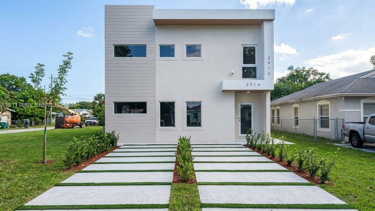 Modern two-story exterior featuring a smooth stucco finish, horizontal siding accents, expansive rectangular windows, and a paved concrete driveway with integrated turf strips
