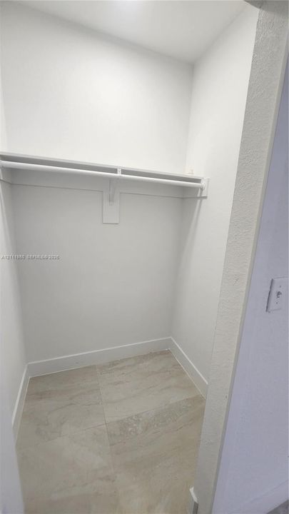 Reach-in closet featuring large-format neutral tile flooring and a built-in shelving system with an integrated clothes rod