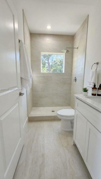 Walk-in shower featuring floor-to-ceiling tile surround and recessed window, paired with a white vanity and stone-composite countertop