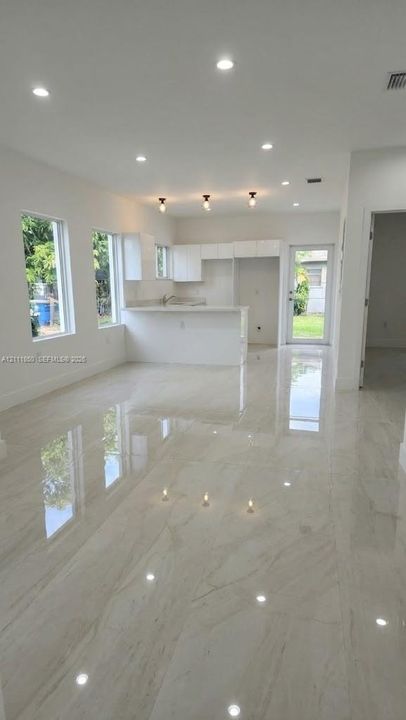 Polished large-format tile flooring, white cabinetry, recessed lighting, pendant fixtures, and a breakfast bar
