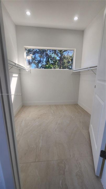 Walk-in closet featuring large-format stone-finish tile flooring, recessed ceiling lighting, horizontal window, and custom wire shelving