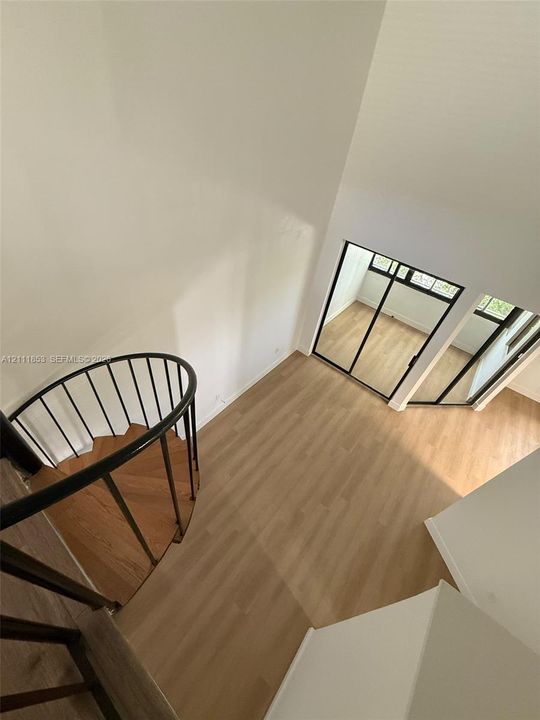 Spiral staircase featuring a black metal railing and wood-finish treads, light-toned wood-finish flooring, and high ceilings with large multi-pane glass enclosures
