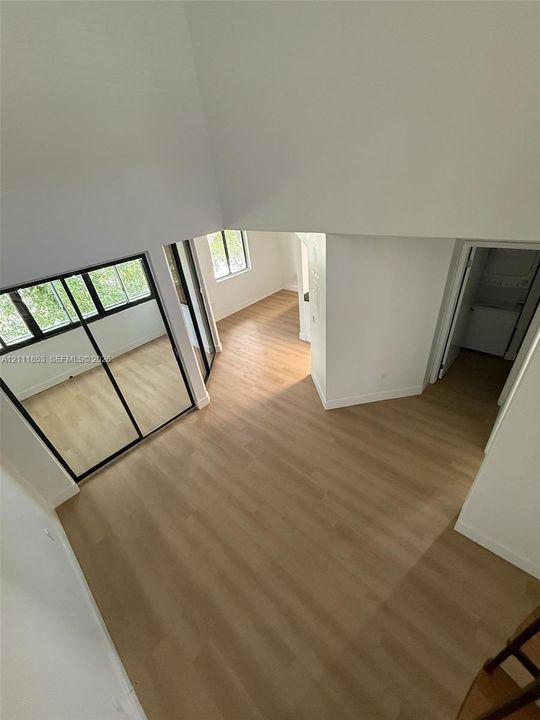 High-ceiling interior featuring wood-finish flooring, sliding mirror-panel closet doors, and multiple windows