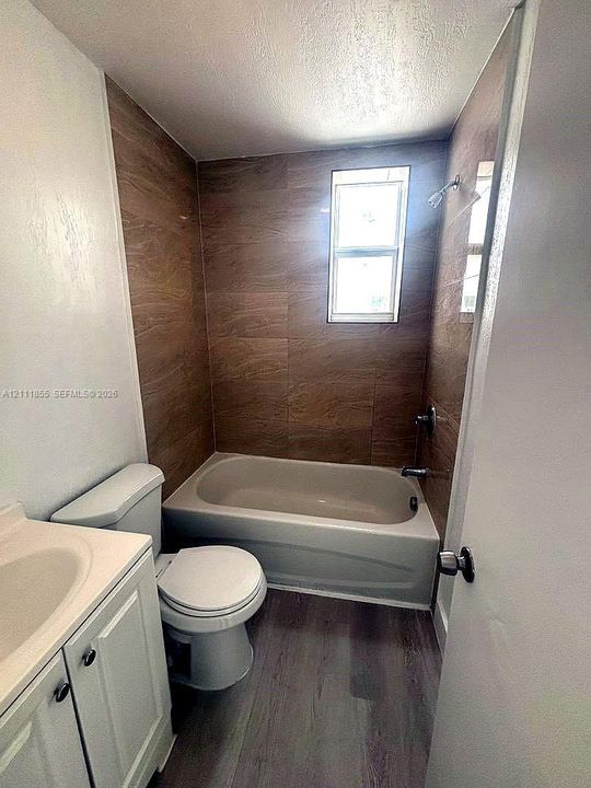 Bathroom featuring wood-finish tile tub surround, white vanity cabinet with an integrated sink, and wood-finish flooring