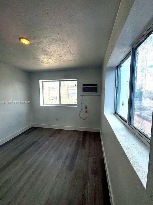 Wood-finish flooring, dual windows with deep sills, and a wall-mounted air conditioning unit