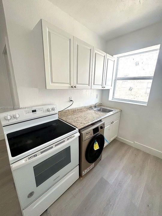Kitchen featuring white shaker-style cabinetry, stone-finish countertops, stainless steel sink, wood-finish flooring, and a glass-top electric range